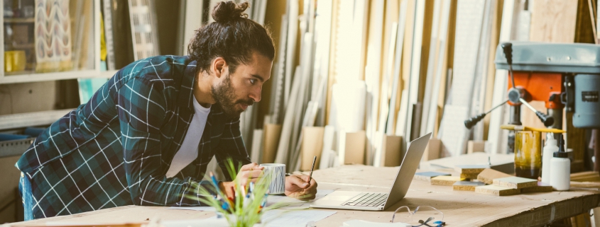 Male business owner working form home and reviewing delivery list on laptop