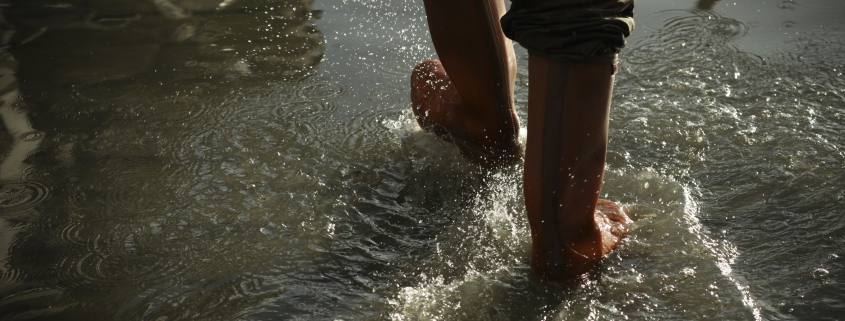 Person with dark coloured rubber boots walking on puddles of water
