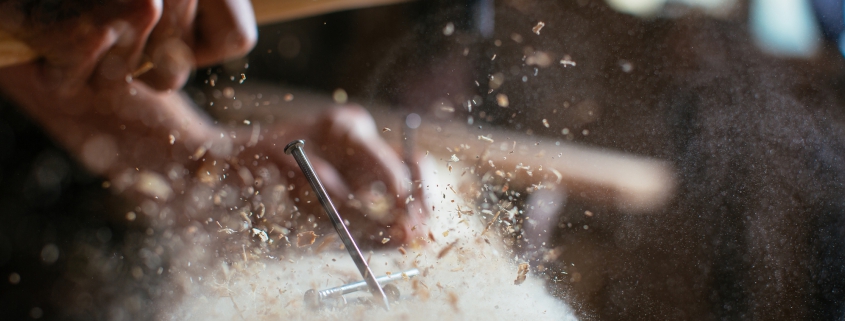 Close up of nail on wooden plank with saw dust floating in background