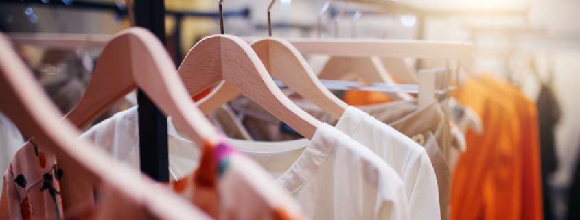 Bright colourful clothes hung with wooden hangers on clothing rack