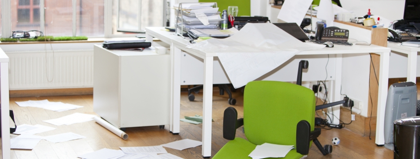 A messy office desk with a green chair knocked over and papers all over the floor.
