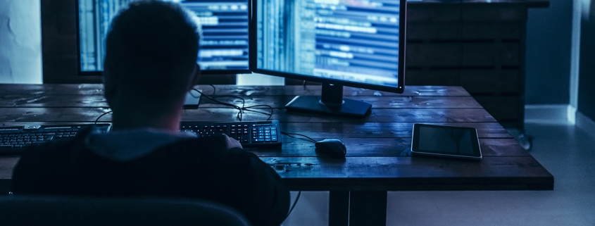 Male computer hacker looking at code on 2 screens