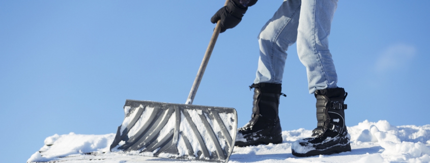 A man shoveling snow off of a roof